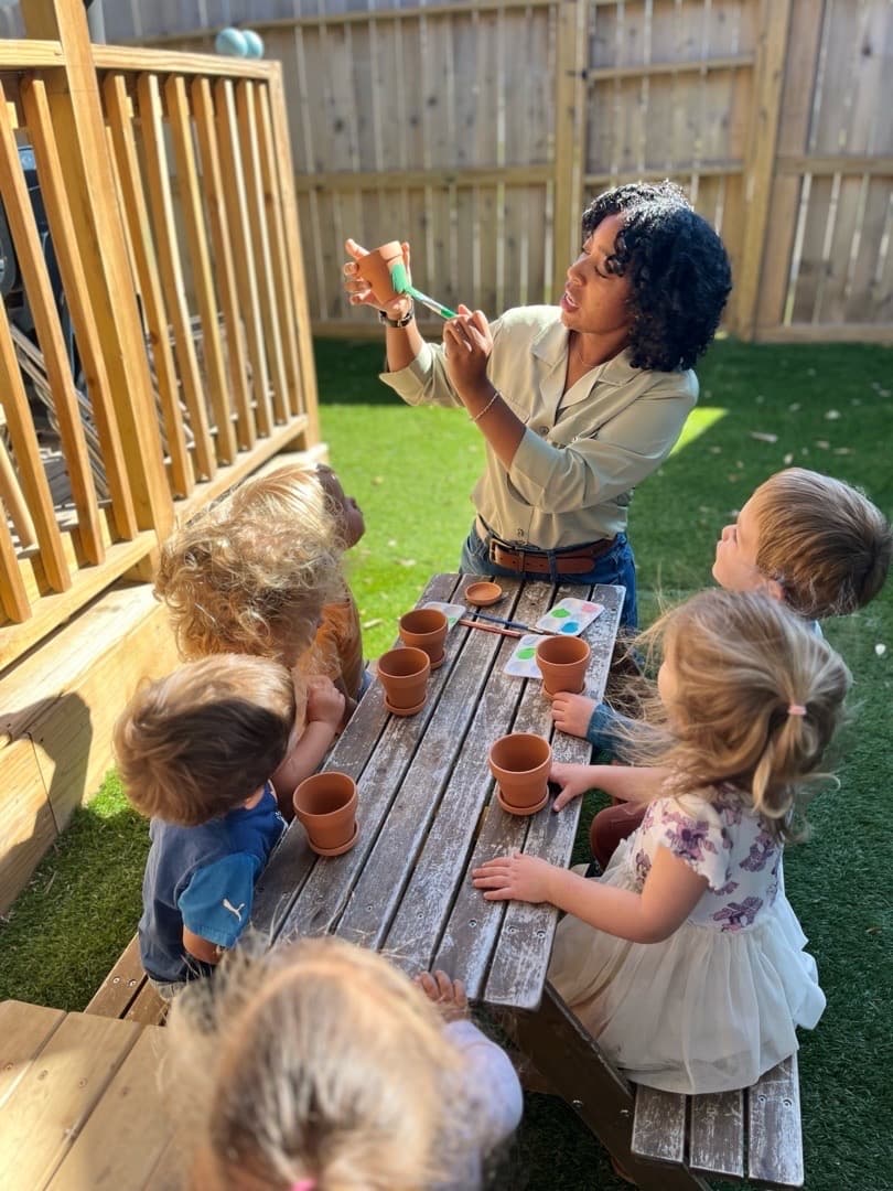Teacher with children painting pots outdoors